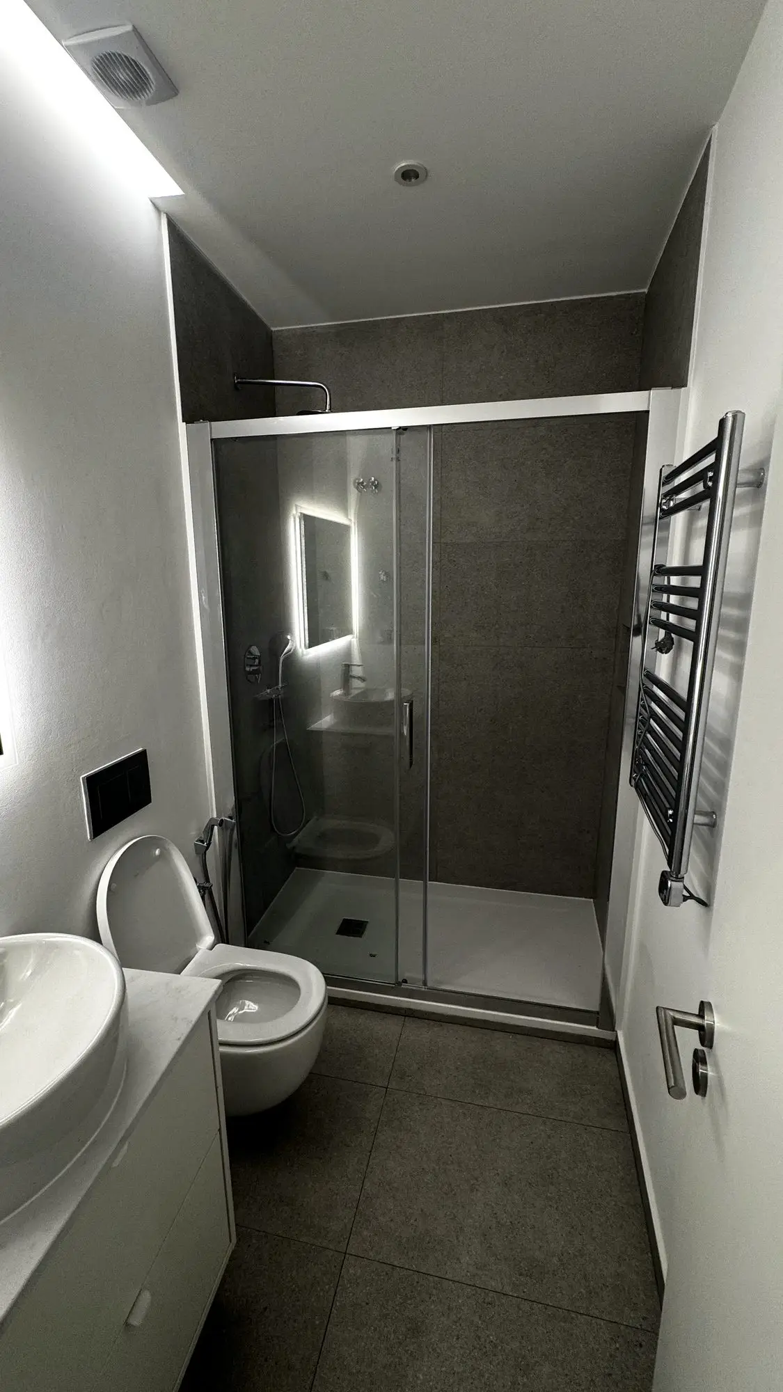 Segunda casa de banho, com base de duche, sanita suspensa e revestimento cerâmico cinzento
