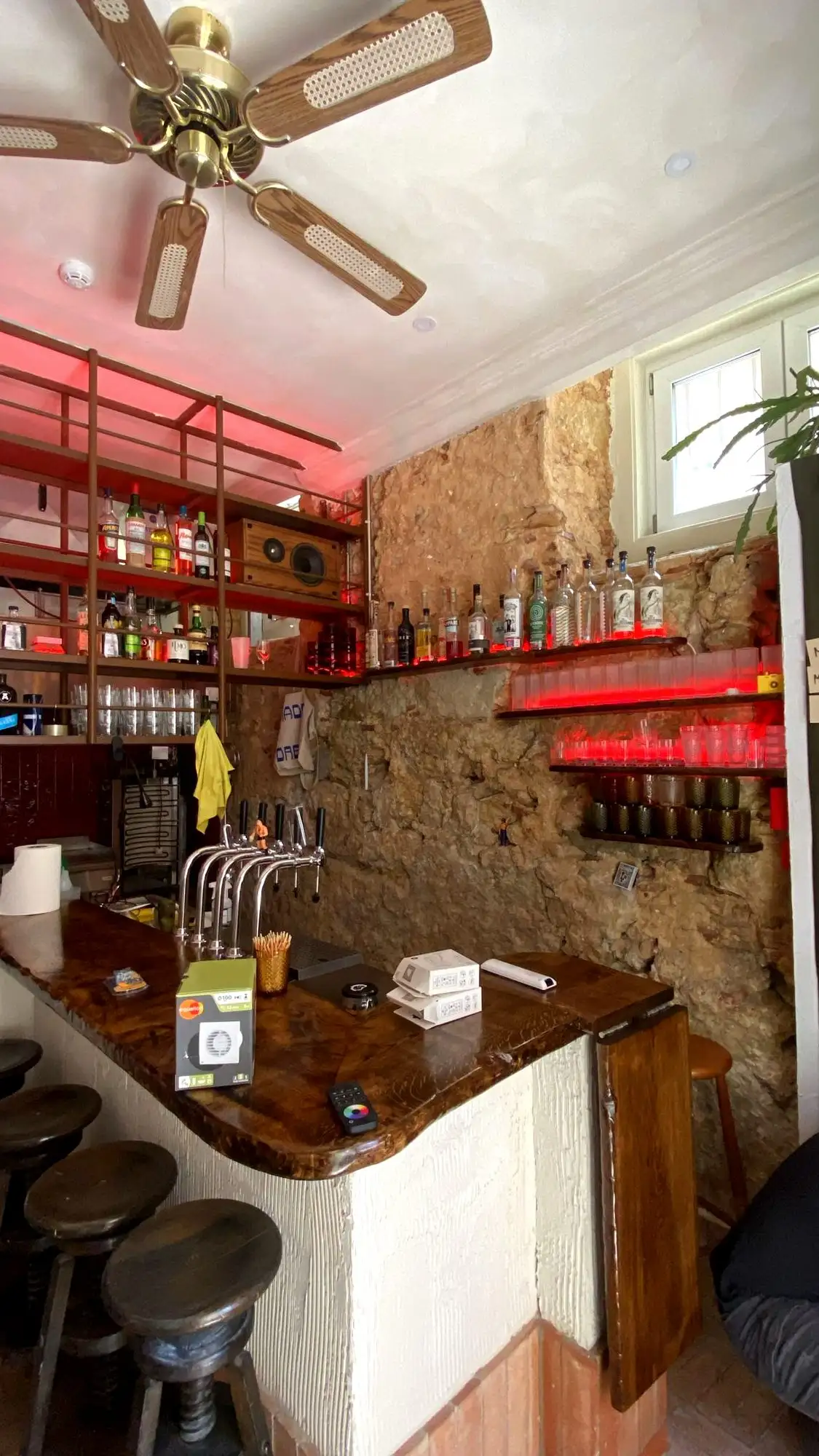 Bar da Bodega Chafa acabado, com iluminação vermelha, garrafeira e balcão em madeira sobre parede de pedra