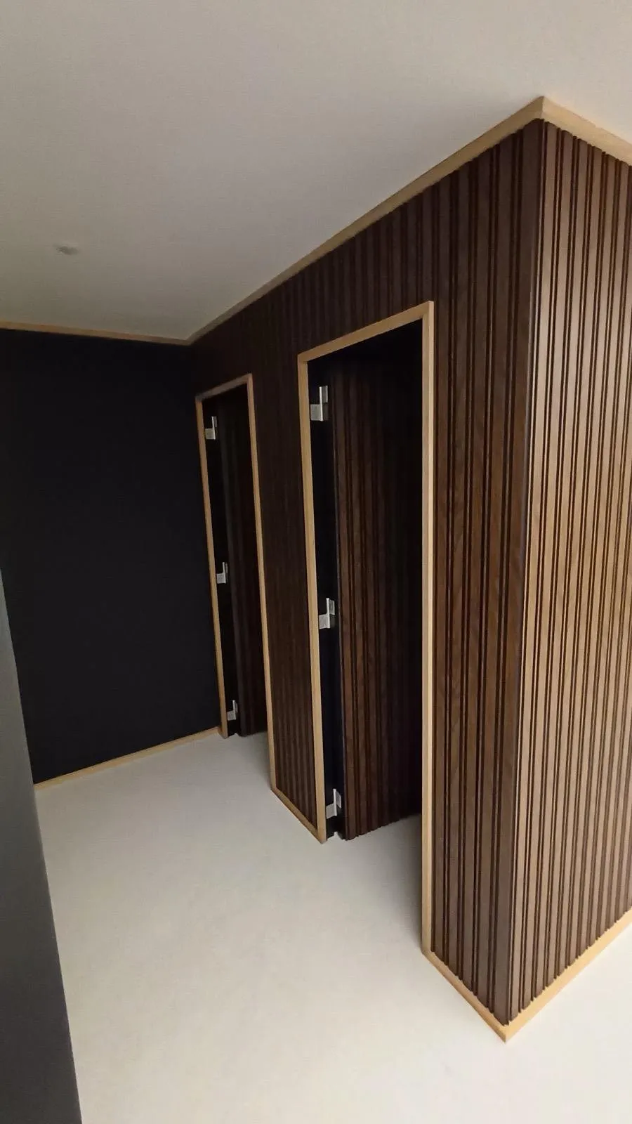 Ripado de parede em madeira escura com portas embutidas, montado pela SUDSTUDIO